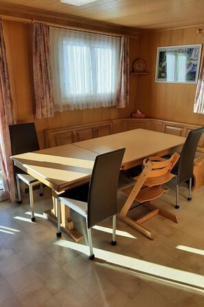 Ein Essbereich mit einem großen Holztisch, sechs Stühlen und einem Fenster mit Vorhängen.