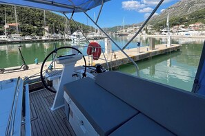 A boat deck with a steering wheel, a lifebuoy, and a view of a marina with boats and buildings. - Dubrovnik Delight: A Sun-Kissed Sailing Experience (Komolac)
