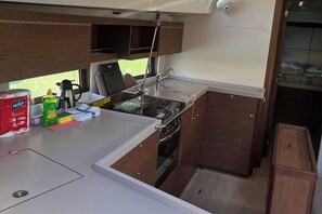 A compact kitchen with a stove, sink, and wooden cabinets. - Dubrovnik Delight: A Sun-Kissed Sailing Experience (Komolac)