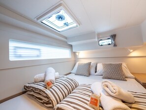 A compact, well-lit room with a skylight, a bed with striped bedding, and a small window. - Sun-Kissed Sailing Adventure in Split, Croatia (Split)