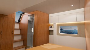 A modern room with a wooden wardrobe, a glass shower, a built-in TV with a sea view, and a small shelf with books. - Sun-Kissed Sailing Adventure in Islas Sarónicas (Alimos)