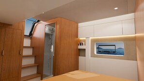 Ein modernes Zimmer mit Holzschrank, Glasdusche, integriertem Fernseher und Meerblick sowie einer kleinen Regalreihe mit Büchern.