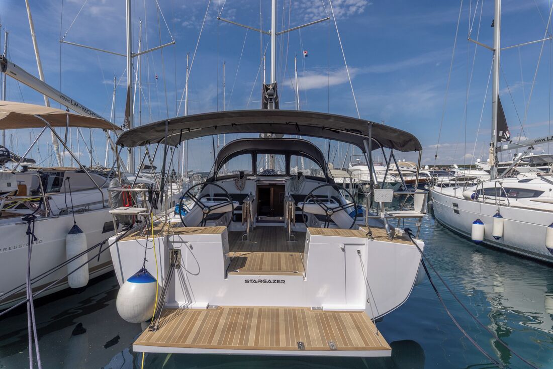 Un yacht était amarré dans une marina, il était doté de plusieurs mâts, d’un pont couvert et d’un volant de direction central.