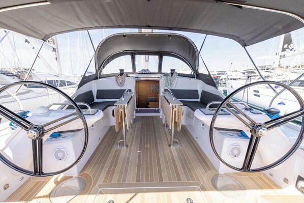 Ein Bootsdeck mit zwei Steuerhörnern, einer zentralen Konsole und Blick auf andere Boote im Hafen.