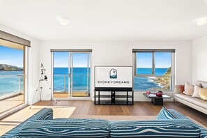 A modern living room with a large window overlooking the sea, a telescope, and a sofa with striped cushions. - Oceanfront Bondi Escape with Spectacular Views (Bondi)