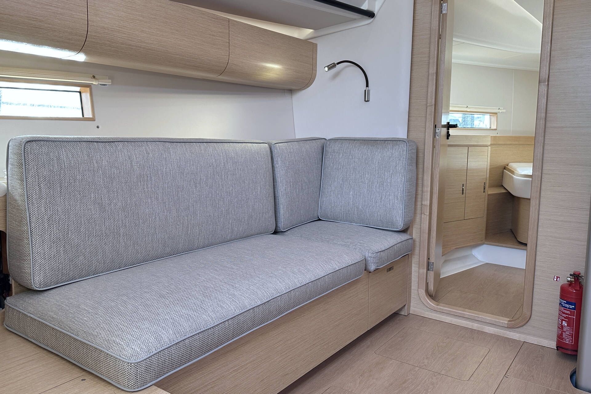 A compact, modern interior with a grey sofa, a wooden cabinet, and a bathroom visible through a door.
