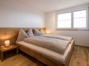 Une chambre à coucher avec un lit en bois, deux tables de chevet, une commode et une fenêtre avec des stores.