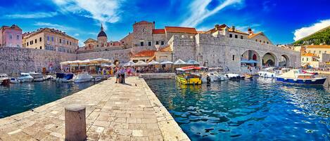 A historic waterfront with stone buildings, a dock with boats, and a paved walkway.