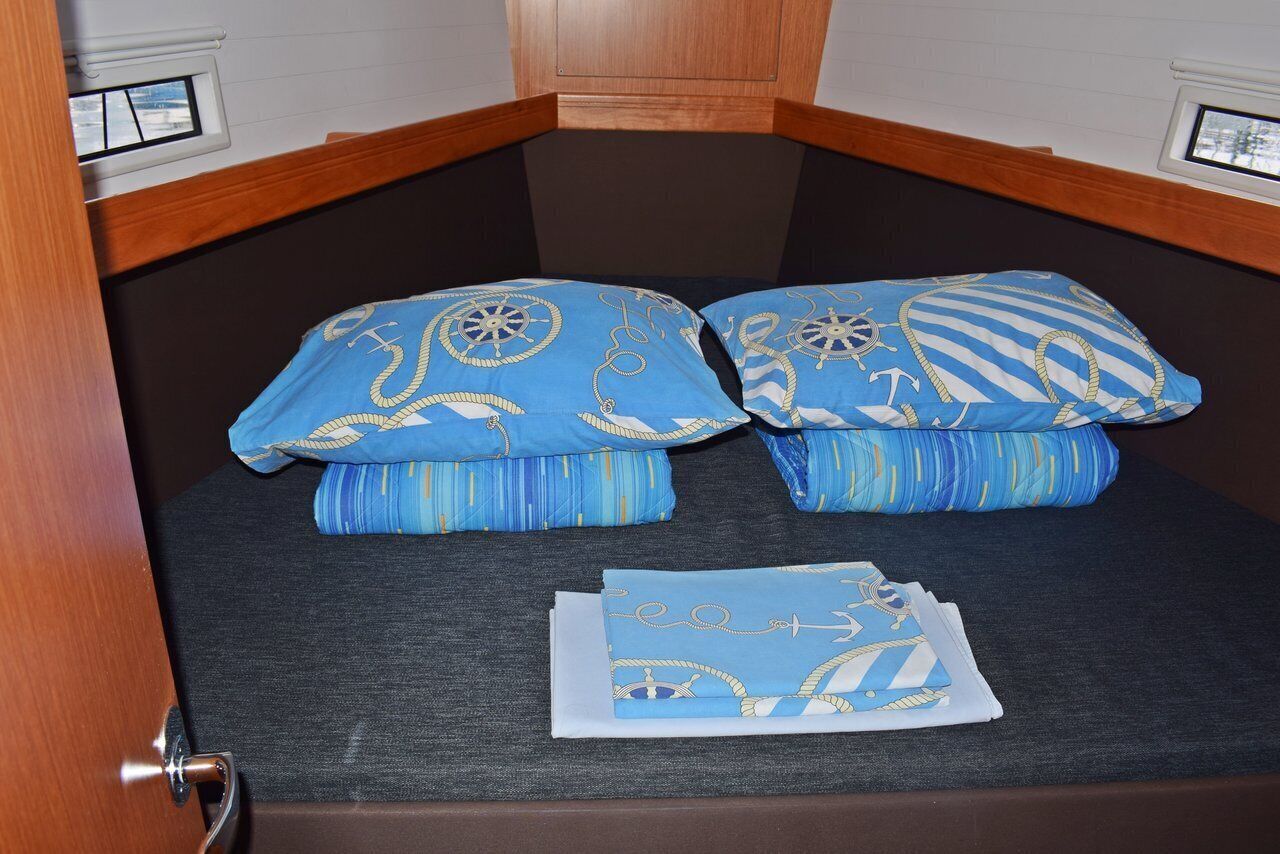Une petite chambre accueillante, avec un matelas marron foncé, deux coussins bleus ornés de motifs marins et une couverture bleue et blanche à rayures, soigneusement pliée.