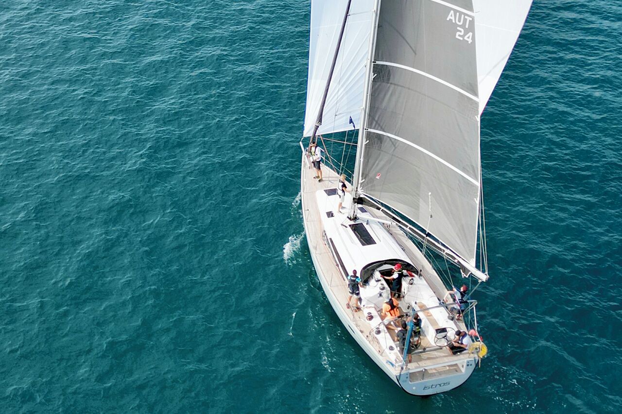 Un voilier à la coque et aux voiles blanches, naviguant sur une eau turquoise.