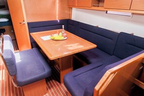 A compact cabin with a wooden table, blue cushioned seating, and a small window. - Sun-Kissed Sailing Adventure in Islas Sarónicas (Alimos)