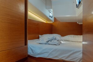 A compact, wooden-furnished room with a bed, a small table, and a ceiling-mounted light fixture. - Sun-Kissed Sailing Adventure in the Dodecanese Islands (Kos)