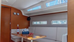 Interiør på en lystbåd med spiseplads, en flaske vin, glas, tissues og et ur.