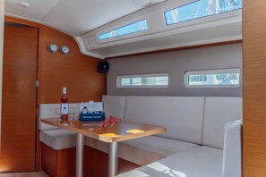 A yacht interior with a dining area, a bottle of wine, glasses, a box of tissues, and a clock. - Sun-Kissed Sailing Adventure in the Dodecanese Islands (Kos)