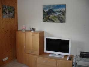 Ein Zimmer mit einem Holzkasten, einem Flachbildfernseher und einem Bild an der Wand.