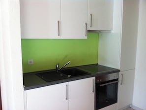 Eine kompakte Küche mit weißen Schränken, einer schwarzen Arbeitsplatte, einem Edelstahlspülbecken und einem eingebauten Backofen.