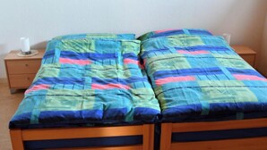 Un lit double avec une courtepointe aux couleurs vives, une table de chevet en bois avec une lampe et un mur sobre.