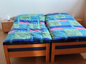Ein Doppelbett mit einer farbenfrohen Steppdecke, ein Nachttisch aus Holz mit einer Lampe und eine schlichte Wand.