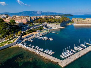An aerial view of a coastal town with a marina, buildings, and a mountainous backdrop.