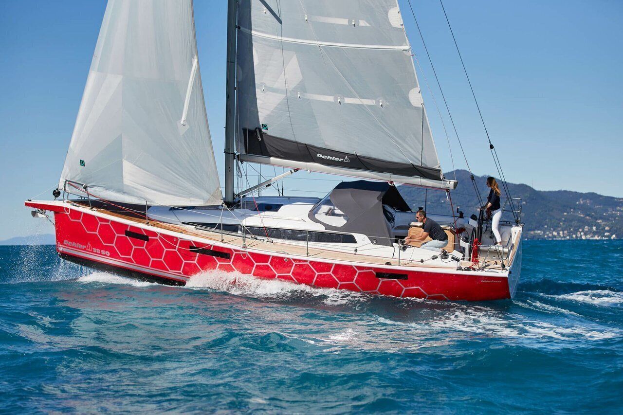 Un voilier rouge et blanc avec deux voiles, un cockpit et une personne debout à la poupe.