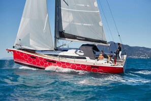Een rode en witte zeilboot met twee zeilen, een kajuit en een persoon die bij de achterkant staat.