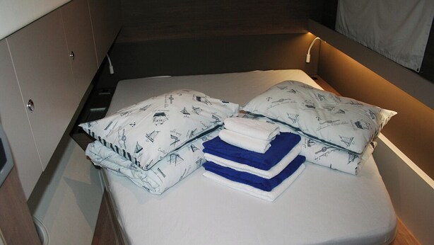 A compact bed with patterned pillows and folded blankets in a small room with wooden walls and a built-in bench. - Dubrovnik Delight: A Sun-Kissed Sailing Experience (Komolac)