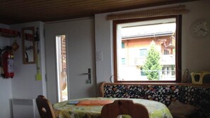 Ett rum med ett matbord, stolar, ett fönster med utsikt över byggnader, en brandsläckare och en klocka på väggen.