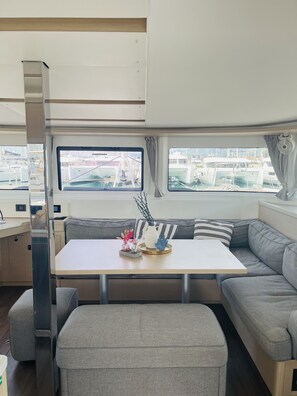 A cozy interior with a table, cushioned seating, and a view of boats through windows. - Sun-Kissed Sailing Adventure in Split, Croatia (Kaštel Gomilica)