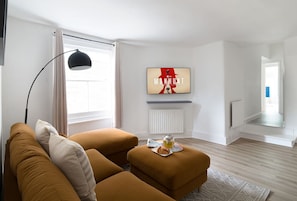 Un saló modern amb un sofà, un otomà i un televisor de pantalla plana muntat a la paret.