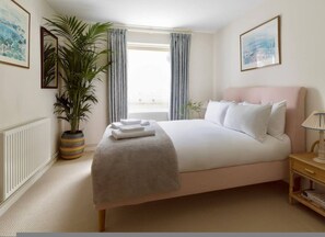 A bedroom with a bed, a bedside table, a lamp, a potted plant, and a window with curtains. - Colourful House 2 Bedroom Apt - Notting Hill (London)