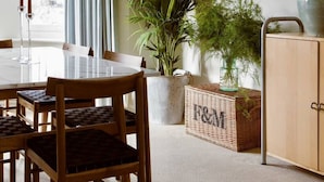Un coin repas comprenant une table, des chaises, une plante en pot, un meuble et un tableau accroché au mur.