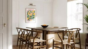A dining area with a wooden table and chairs, a poster on the wall, and a window with blinds. - Notting Hill Mews House Sleeps 8 (London)