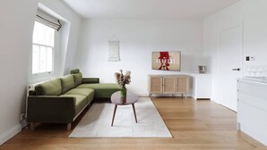 Uma sala de estar moderna com um sofá verde, uma pequena mesa redonda com um vaso, um armário e uma janela grande.