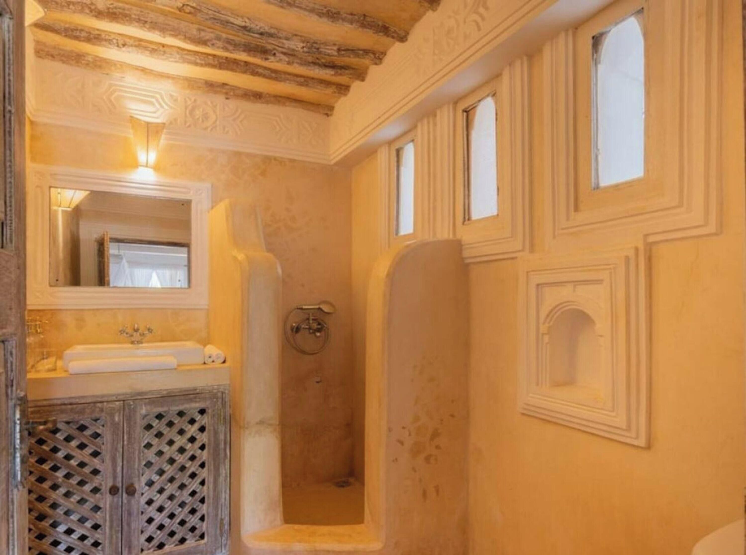 Een badkamer met een houten plafond, een wastafel met spiegel, een douche en decoratieve lijsten.