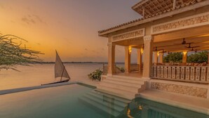 Zona de piscina con un velero, un área de estar techada y vista al agua.