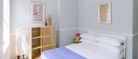 A bedroom with a bed, a wooden wardrobe, a nightstand with a vase, and two framed pictures on the wall.