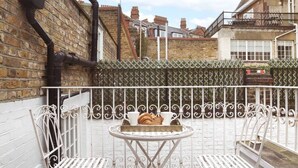 A small outdoor patio with two white metal chairs and a round table, a brick wall, and a metal fence. - Kings Road Chelsea Sleeps 6 (London)