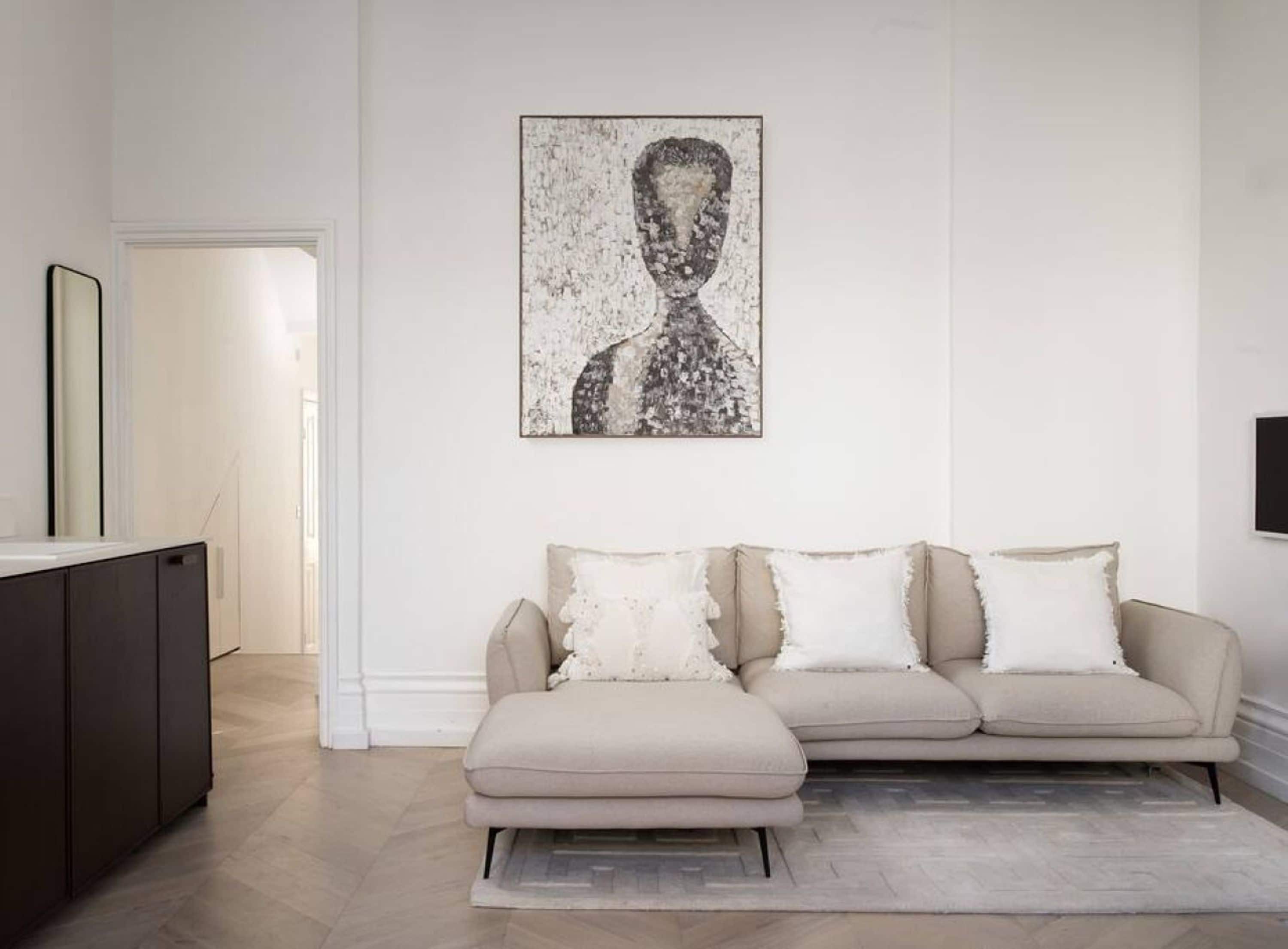 A living room with a sofa, a painting, and a television on the wall.