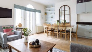 Een woonkamer met een bank, een bijzettafeltje en een eethoek met een tafel en stoelen.