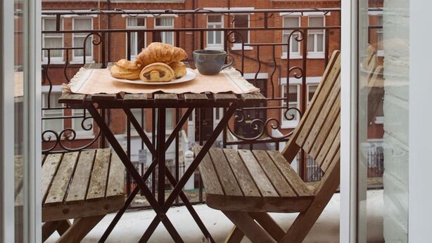 Een balkon met een tafel, een stoel en uitzicht op rode bakstenen gebouwen.
