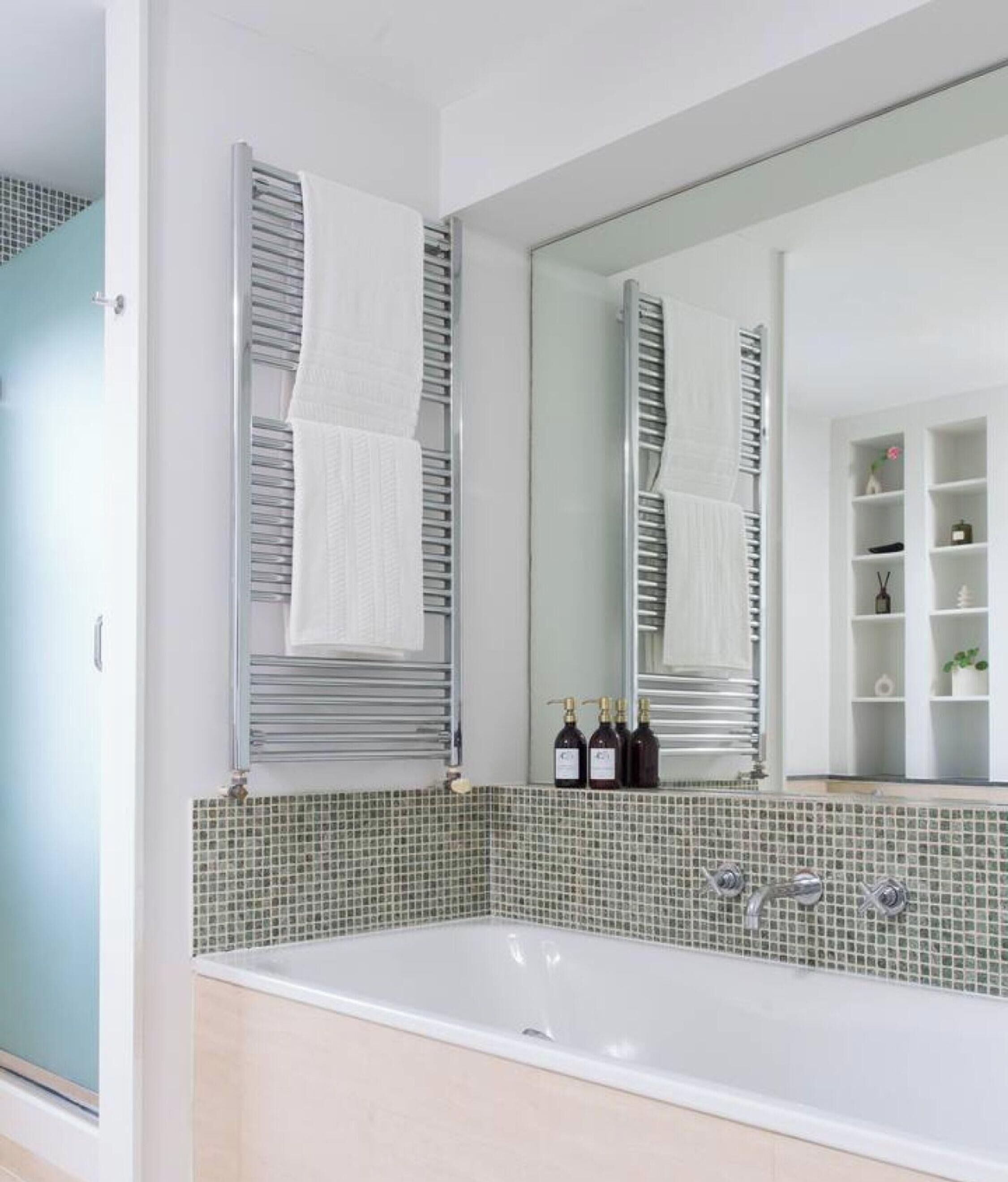 A bathroom with a large mirror, a bathtub, and a tiled backsplash.