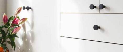 A white wardrobe with black handles, a wooden stool, and a potted plant with pink leaves.