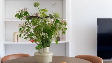 A round dining table with six chairs, a vase with flowers, and a plate of cookies.