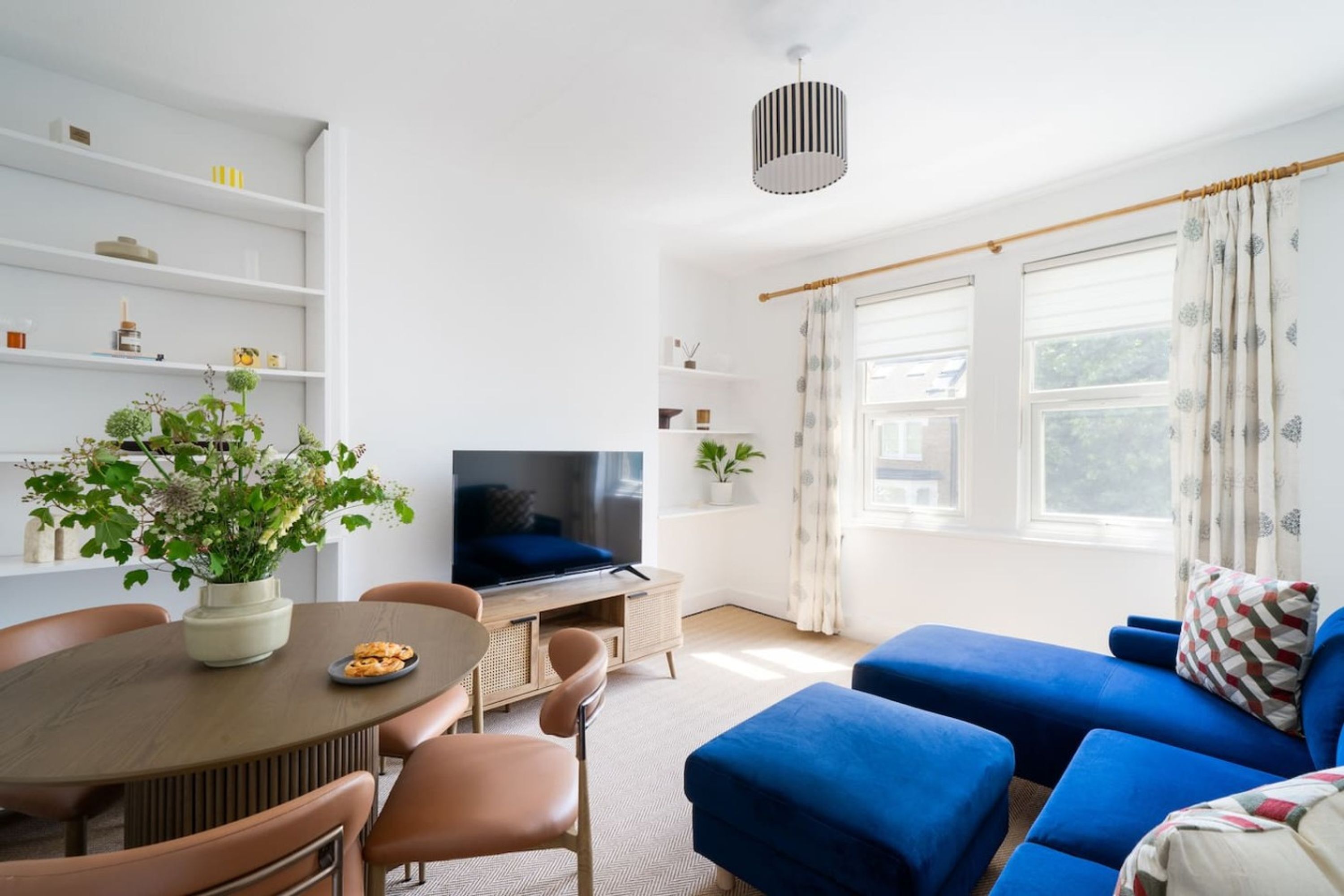 A modern living room with a TV, sofa, dining table, and potted plants.