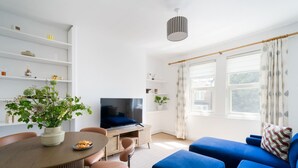 Moderni olohuone, jossa on televisio, sohva, ruokapöytä ja ruukkukasveja.