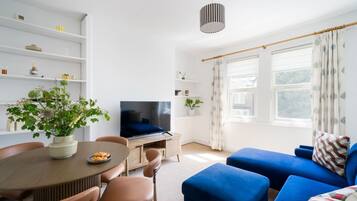 A modern living room with a TV, sofa, dining table, and potted plants.