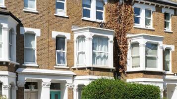 A row of terraced houses with a green door, a hedge, and a parked car.