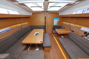 Ein Yacht-Interieur mit einem zentralen Tisch, gepolsterten Sitzgelegenheiten, Dachfenstern und einer Karte an der Wand.