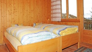 Ein Schlafzimmer einer Holzhütte mit einem Doppelbett, einem Fenster mit Vorhängen und einer Pendelleuchte.