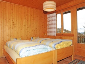 A wooden cabin bedroom with a double bed, a window with curtains, and a hanging light fixture.